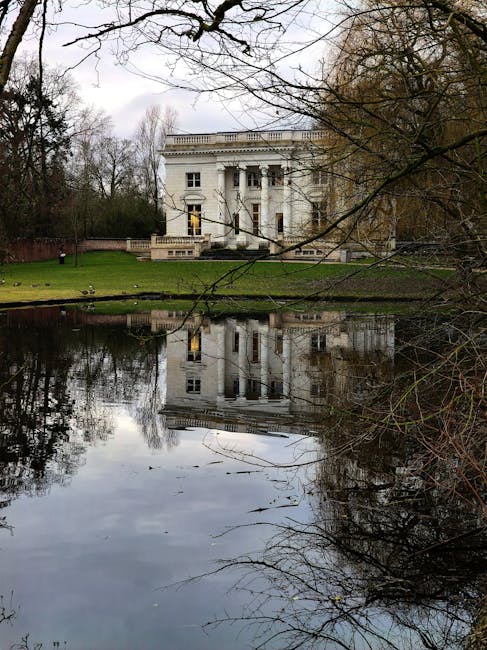 A wide shot of Gunnersbury Park showcasing the large, historic mansion with multiple wings and symmetrical windows, set against a bright blue sky with a few scattered clouds. The mansion is painted in a pale yellow tone and features classical architectural elements. In the foreground, an expansive, well-maintained green lawn extends toward the building, providing open space typical for outdoor events or leisure. To the sides and behind the mansion, dense trees form a natural backdrop, with the surrounding environment appearing calm and sunny. This outdoor scene is ideal for illustrating house removals or furniture transport processes, highlighting the spacious outdoor environment often involved in residential or commercial relocations. Man with Van Gunnersbury may occasionally operate in settings like this, supporting home relocation, packing, and loading activities involving exterior areas and estate grounds.