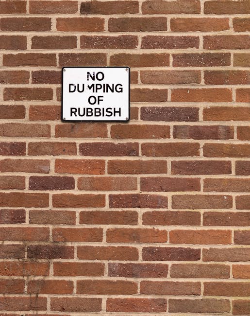 A close-up of a wooden gate with a warning sign attached, situated in a green outdoor setting. The sign has a red and white header with the word 'WARNING' in bold, capital letters, followed by black text that states, 'ANYONE WHO TIPS RUBBISH ON THESE ALLOTMENTS WILL BE PROSECUTED,' and is signed by Order Lea and Clevendon Parish Council. Behind the gate, there is a well-maintained garden with raised vegetable beds, some covered with black fabric protectors, and a green plastic watering can. In the background, lush trees, a grassy lawn with small white flowers, and a partly cloudy sky are visible, indicating a peaceful, rural environment that may be related to community gardening or allotments, often requiring moving and transportation services for equipment and supplies.