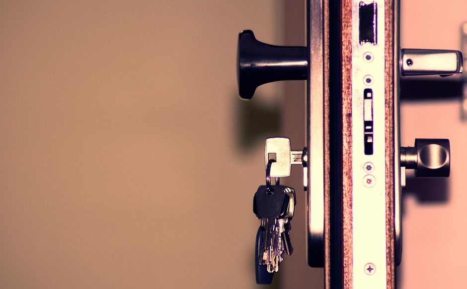 Close-up of a door lock with a key inserted, situated on a wooden door frame. The keys are attached to a small keyring and hang to the side of the lock. The door lock mechanism is metallic, with visible keyhole, latch, and locking components. The door appears to be inside a residential property, as indicated by the nearby door handle and the surrounding wooden and hardware features. The image shows part of a larger home interior, emphasizing the importance of secure locking during house removals. The background is blurred, focusing attention on the lock and keys, which are relevant to house relocation and safe access during moving processes. The scene visually supports the context of potential access issues or lost keys during home moving, as handled by companies like Man with Van Gunnersbury, specialists in removals and transport services.